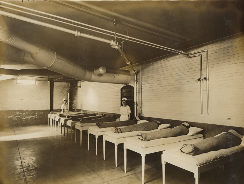 There are several patients lined up on beds who are wrapped in dry packs. Their faces are covered with a towel, and two nurses are present.