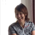 Head and shoulders shot of smiling apparent woman with dark hair, wearing cycling shirt.