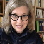 Head and shoulders shot of blond apparent woman with dark glasses smiling.