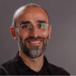 Head and shoulders of apparent smiling man with dark beard and glasses.